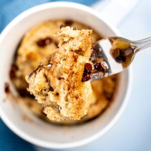 A fork lifting a piece of banana mug cake out of the mug with cinnamon and mini chocolate chips on top.