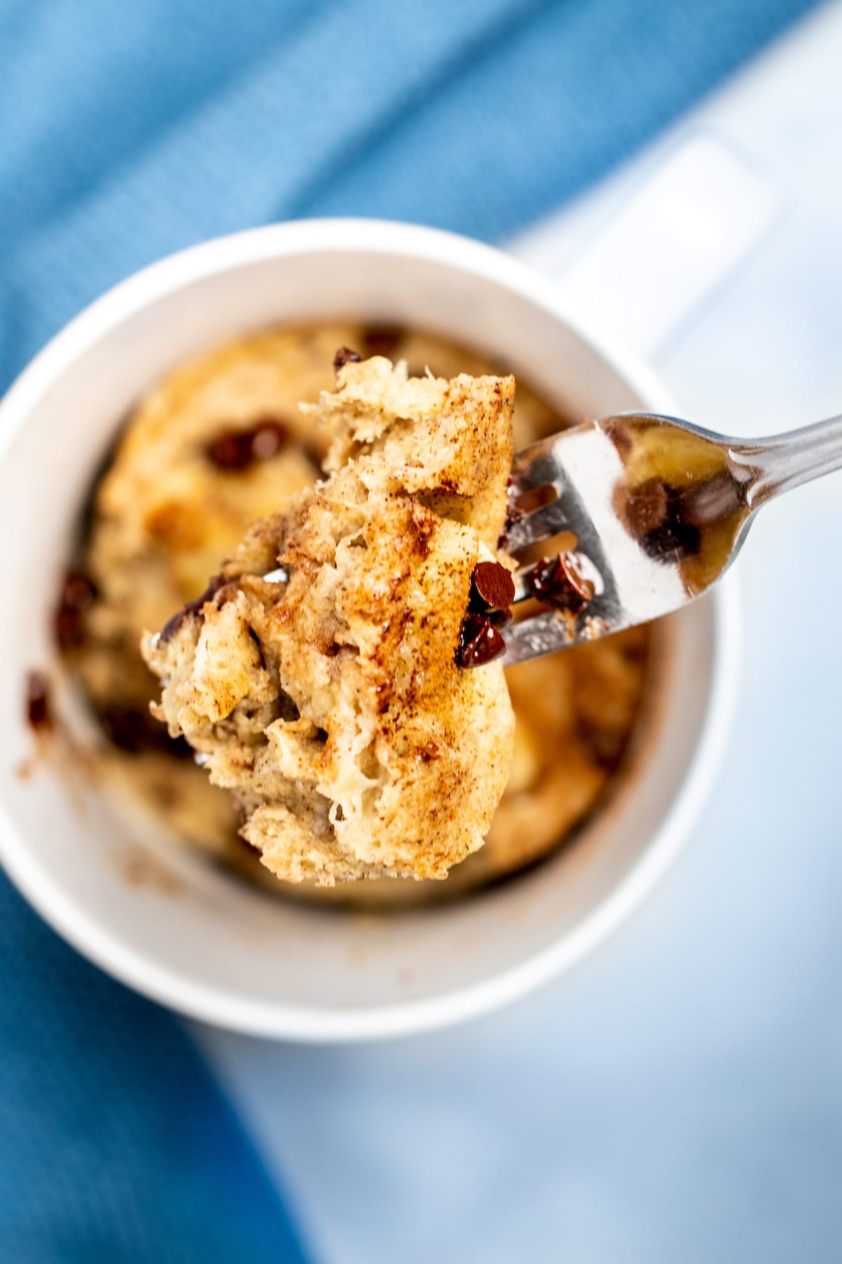 A fork lifting a piece of banana mug cake out of the mug with cinnamon and mini chocolate chips on top.