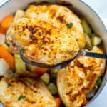 Chicken breast over potatoes and carrots in a dutch oven, with a spatula lifting one up.