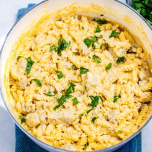 A dutch oven resting on a kitchen towel on the table, full of garlic parmesan chicken pasta topped with fresh parsley.