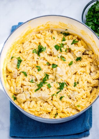 A dutch oven resting on a kitchen towel on the table, full of garlic parmesan chicken pasta topped with fresh parsley.