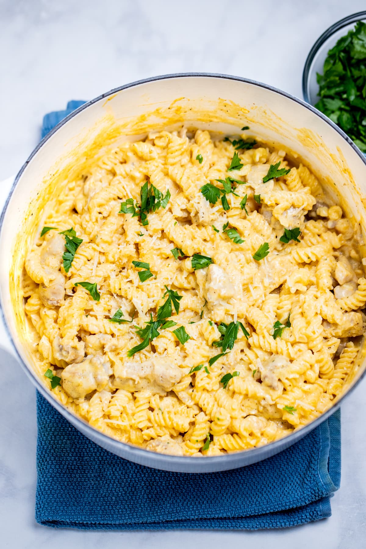 A dutch oven resting on a kitchen towel on the table, full of garlic parmesan chicken pasta topped with fresh parsley.