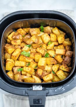 Fully cooked air fryer breakfast potatoes in an air fryer basket, topped with fresh parsley.