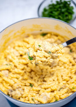 A spoon lifting garlic parmesan chicken pasta out of a dutch oven topped with fresh parsley.