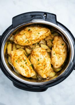 Cooked chicken breast covered in seasoning and fresh parsley, on top of cubed gold potatoes in an instant pot.