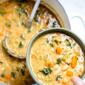 A hand holding a bowl of white bean soup over a pot of soup with a ladle in it.