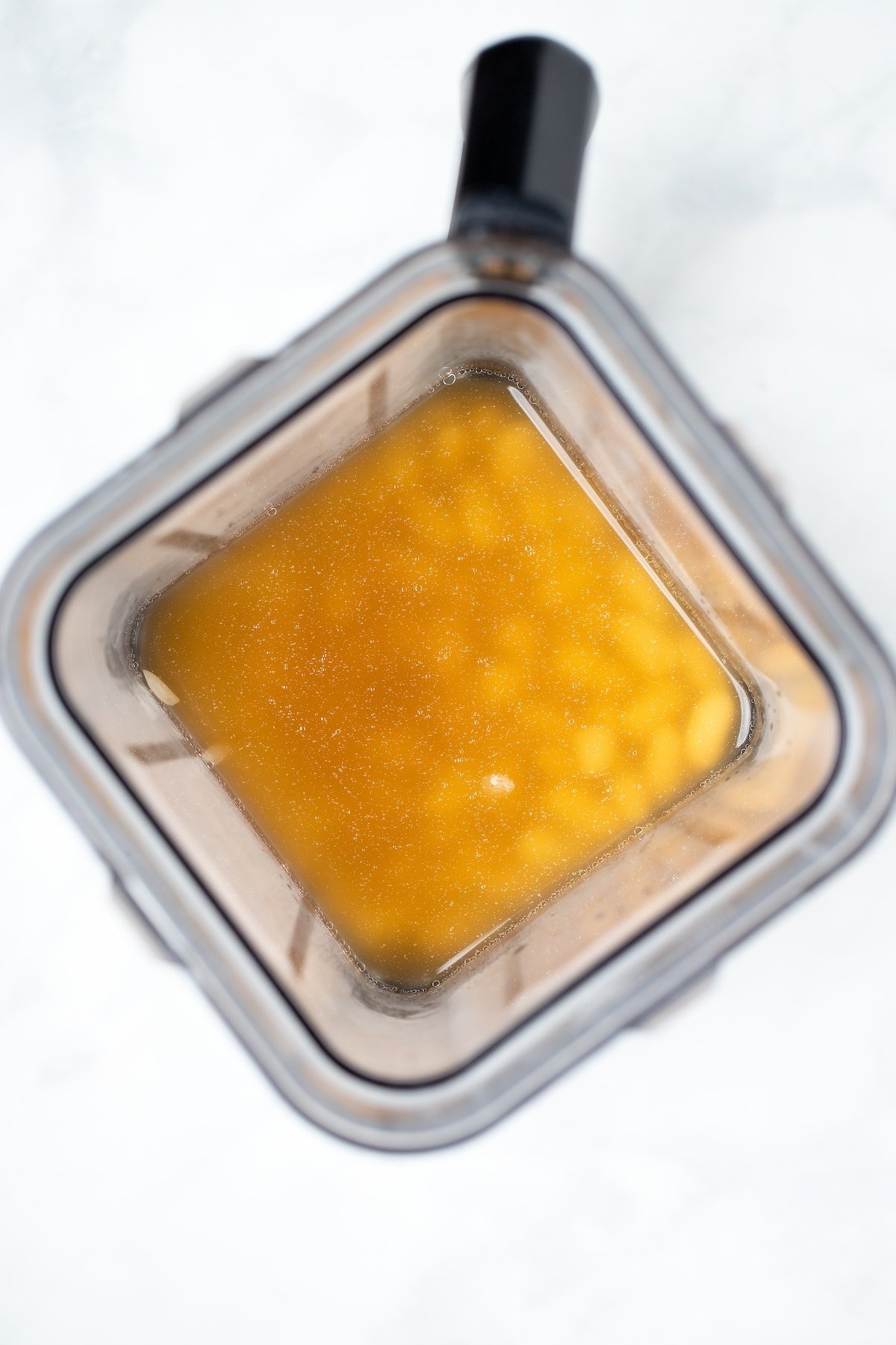 A blender with white beans and broth before blending together.