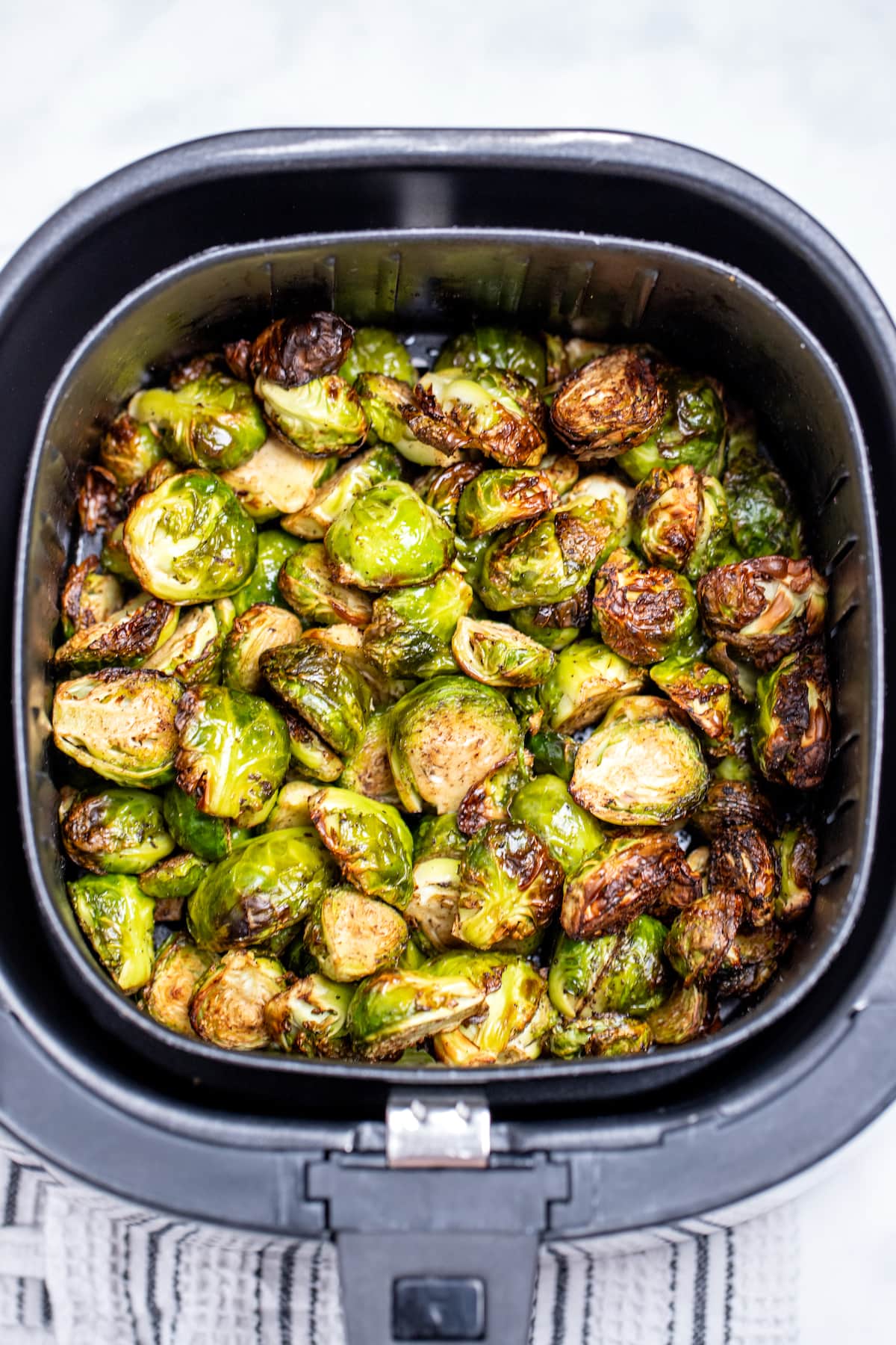 Fully cooked Brussels sprouts in an air fryer basket on a table.
