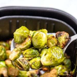 A spatula lifting Brussels sprouts out of an air fryer basket.
