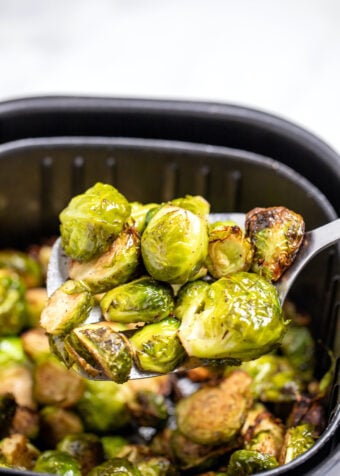 A spatula lifting Brussels sprouts out of an air fryer basket.