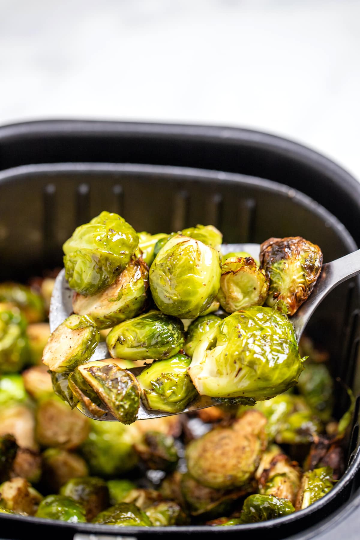 A spatula lifting Brussels sprouts out of an air fryer basket.