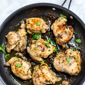 Greek marinated chicken thighs in a skillet topped with fresh parsley.