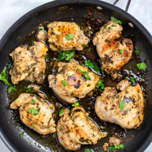 Greek marinated chicken thighs in a skillet topped with fresh parsley.