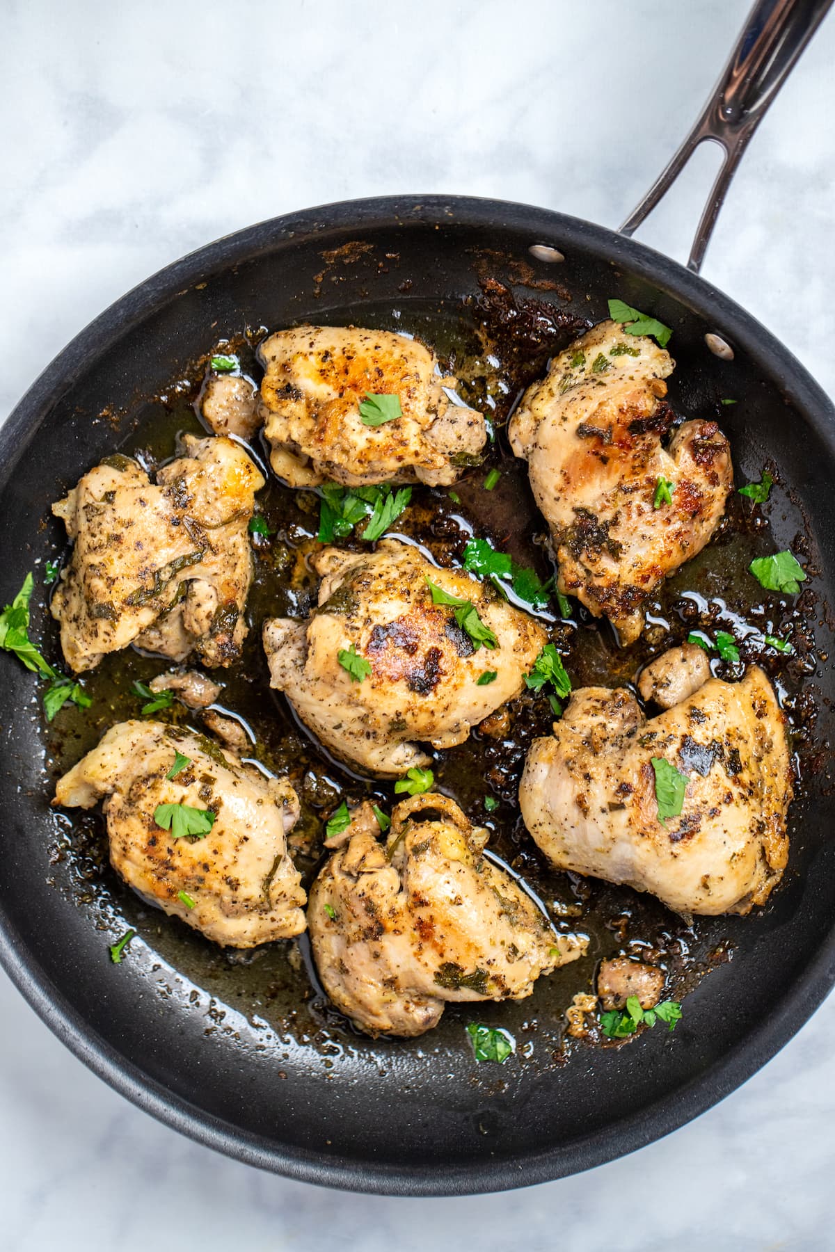 Greek marinated chicken thighs in a skillet topped with fresh parsley.
