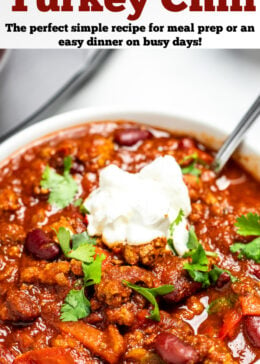 Pinterest pin with a bowl of turkey chili with a spoon topped with sour cream and fresh cilantro.