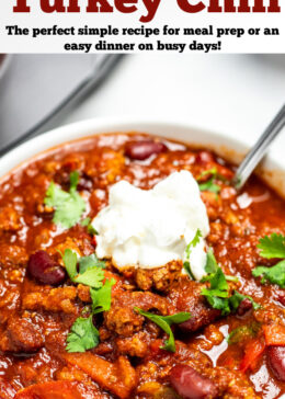 Pinterest pin with a bowl of turkey chili with a spoon topped with sour cream and fresh cilantro.