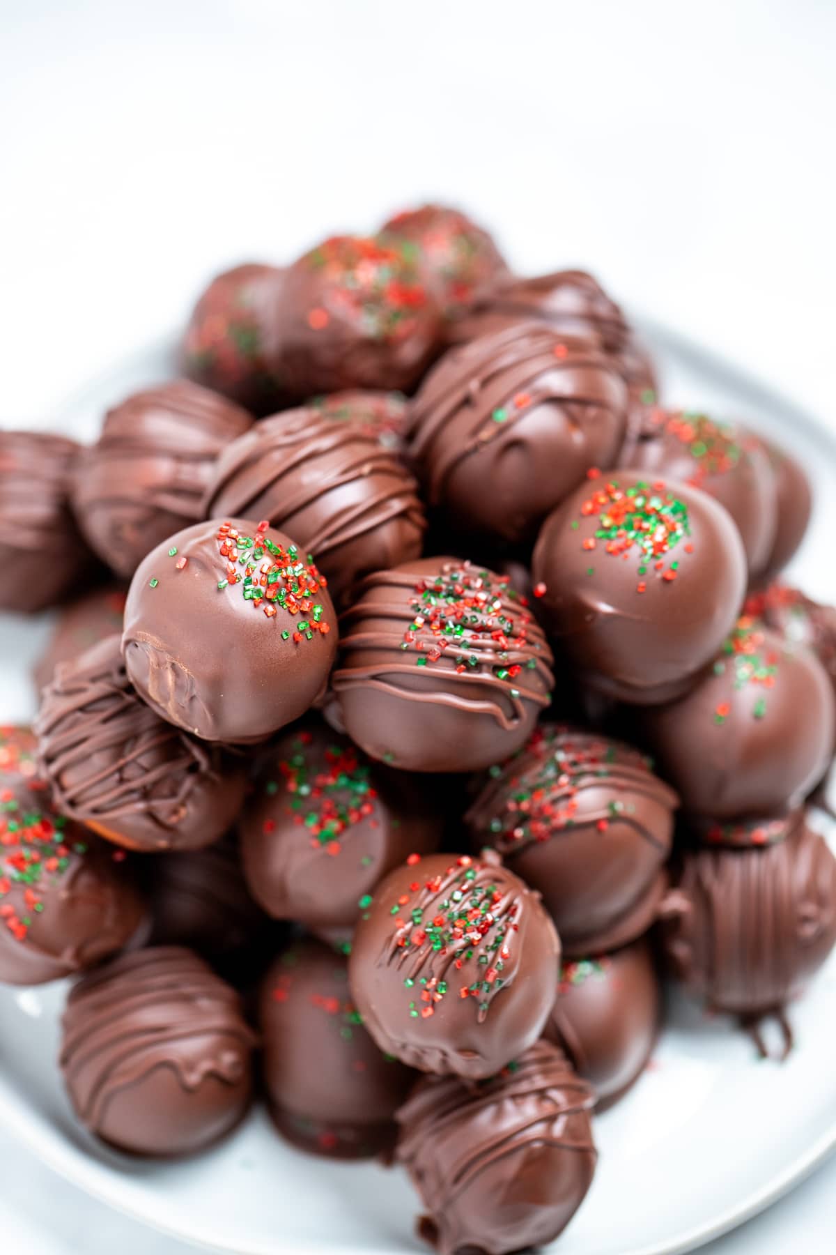 Chocolate covered peanut butter balls topped with drizzled chocolate and sprinkles on a plate on a table.