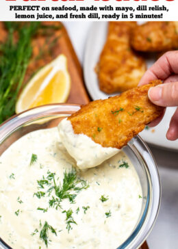 Pinterest pin with a bowl of homemade tartar sauce on a cutting board, topped with fresh dill and a hand dipping a fish stick into the sauce, with a lemon wedge in the background.