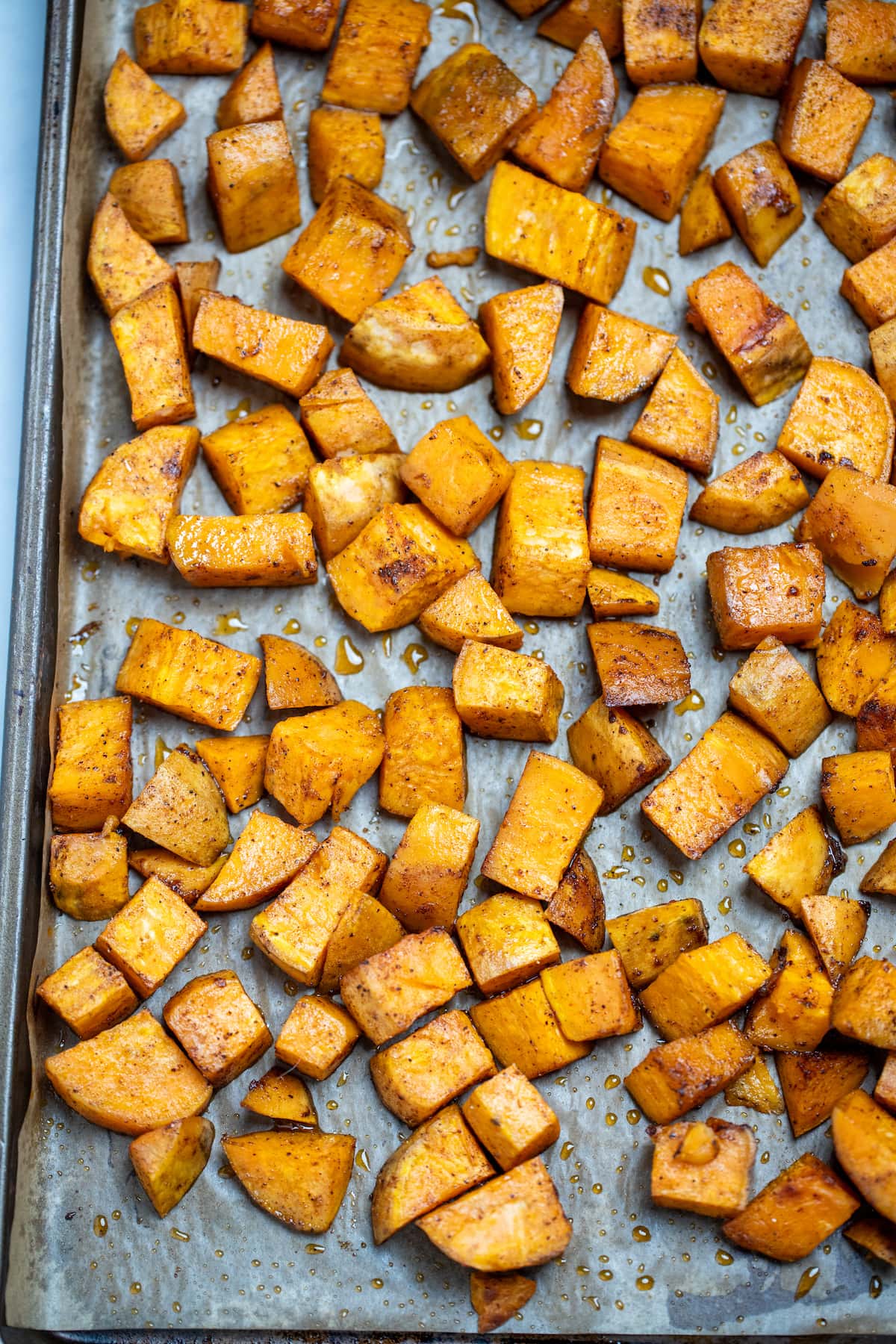 Roasted sweet potato cubes on a sheet pan with parchment paper.