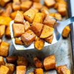 Roasted sweet potato cubes on a sheet pan with parchment paper, being lifted up by a spatula.