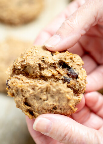 Two hands holding an oatmeal breakfast cookie and breaking it in half to show the chewy cookie center.