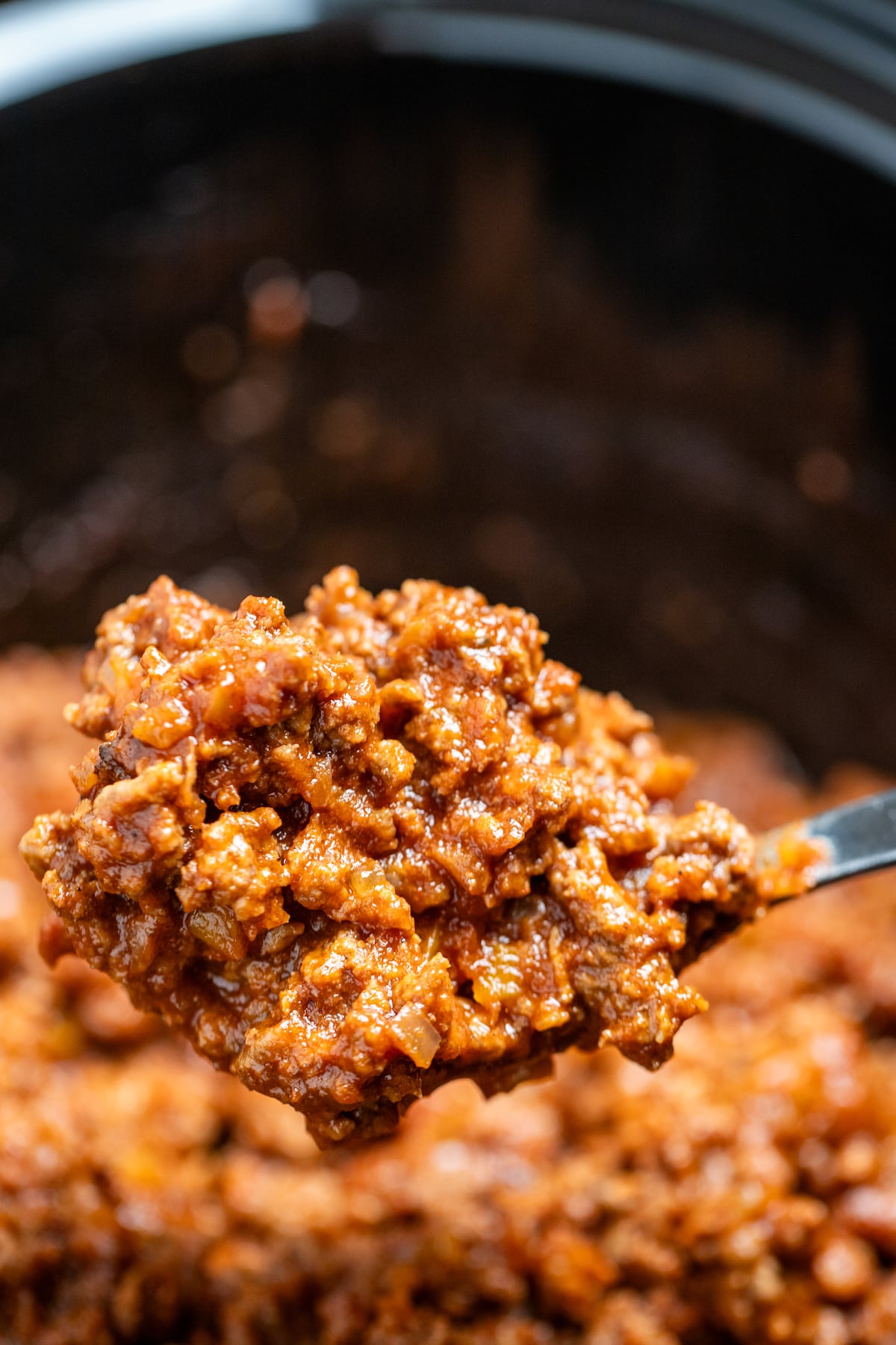A crockpot full of sloppy joes filling with a spoon scooping filling out of the crockpot.