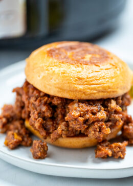 A toasted burger bun full of crockpot sloppy joes on a plate.