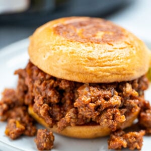 A toasted burger bun full of crockpot sloppy joes on a plate.