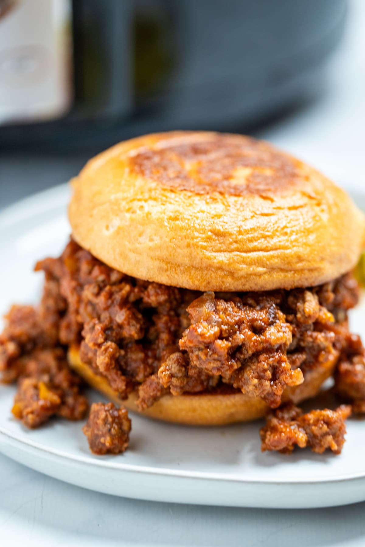 A toasted burger bun full of crockpot sloppy joes on a plate.