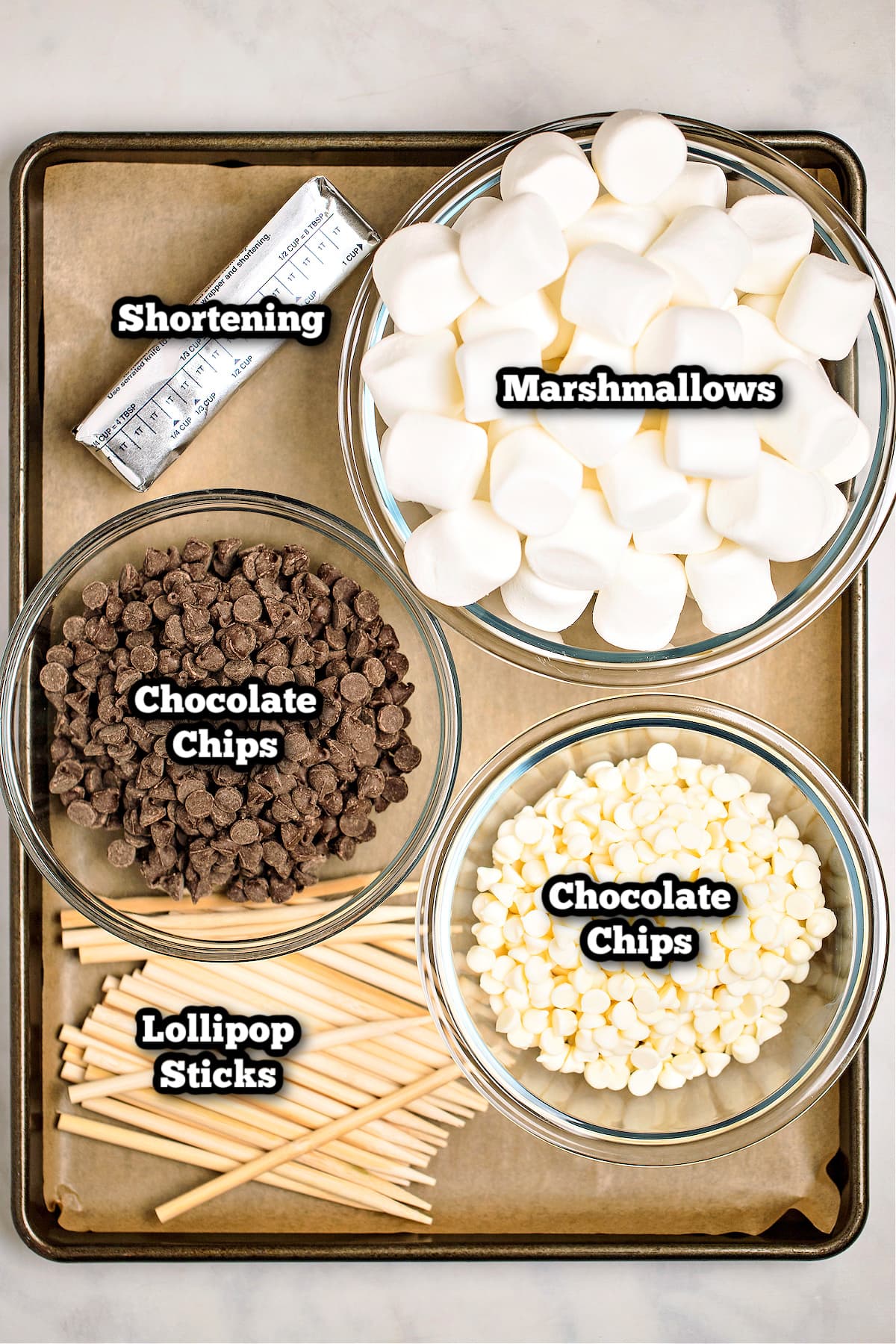 Individual ingredients for chocolate dipped marshmallows on a sheet pan lined with parchment paper on a table.