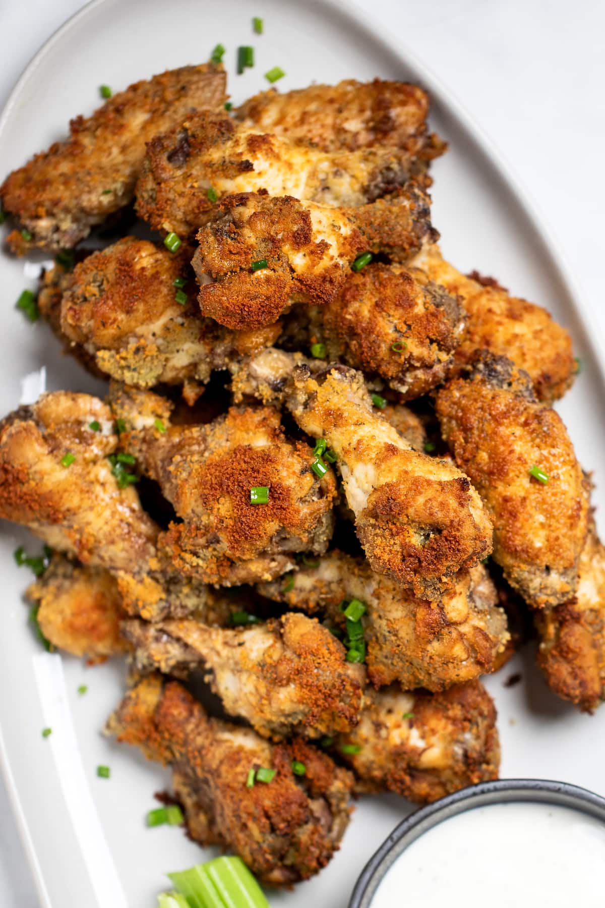 A plate with garlic parmesan wings in a pile topped with chives and next to a bowl of ranch and celery.