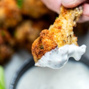 A hand holding a garlic parmesan chicken wing after dipping it in ranch, with more wings in the background.