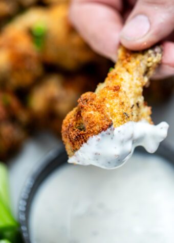 A hand holding a garlic parmesan chicken wing after dipping it in ranch, with more wings in the background.