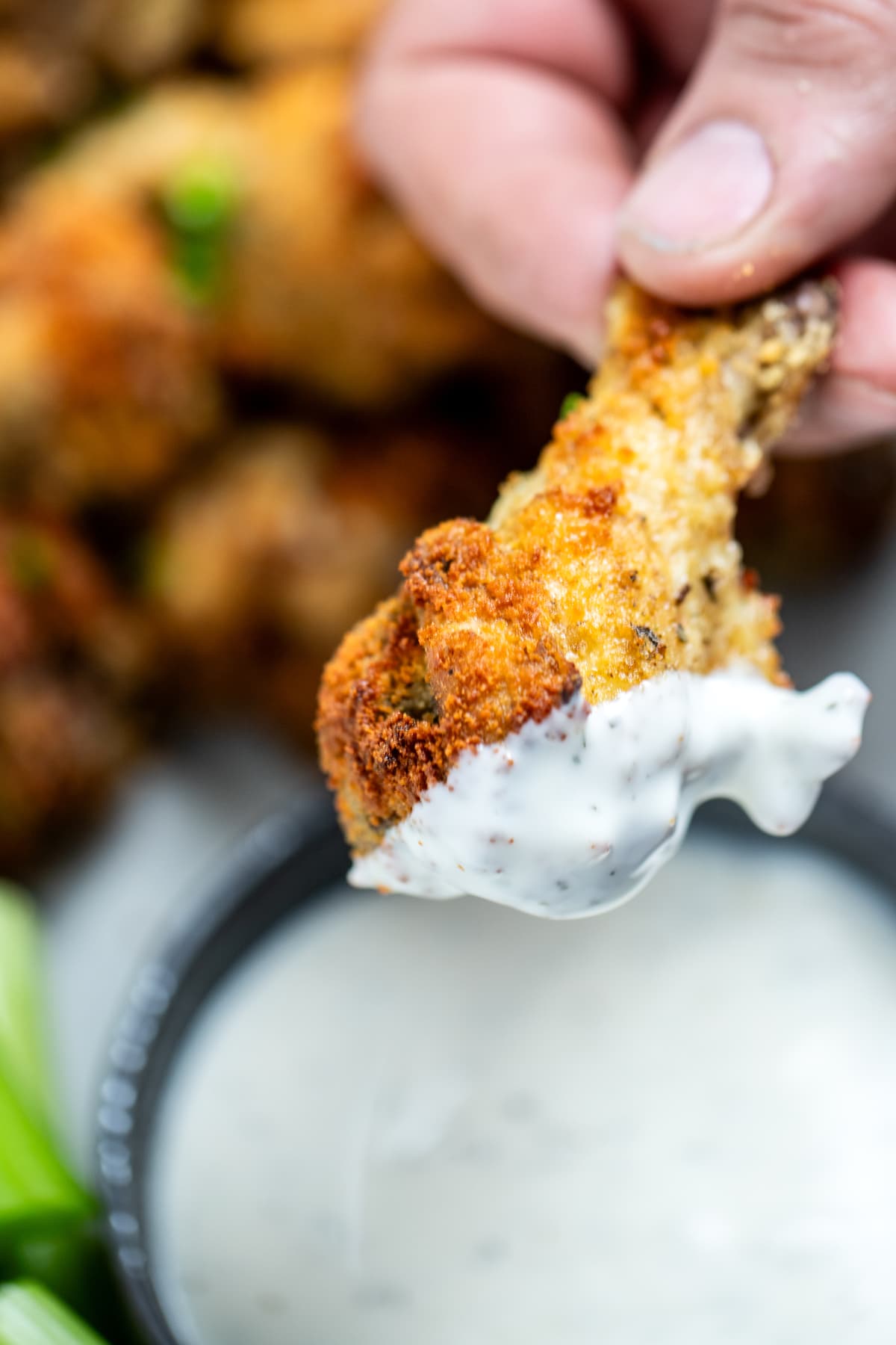 A hand holding a garlic parmesan chicken wing after dipping it in ranch, with more wings in the background.