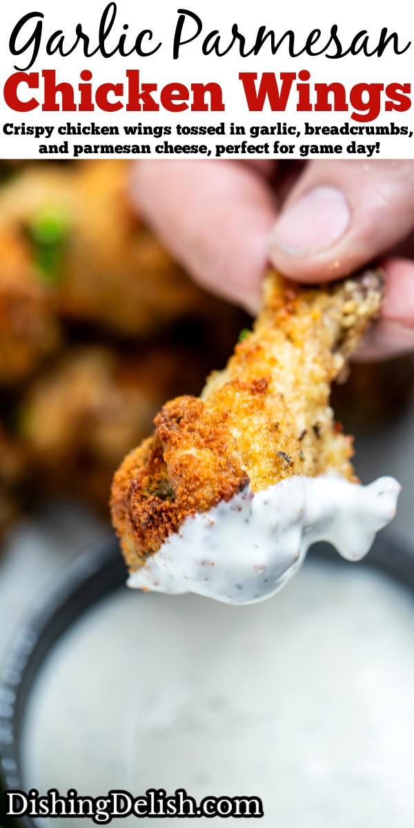 Pinterest pin with a hand holding a garlic parmesan chicken wing after dipping it in ranch, with more wings in the background.