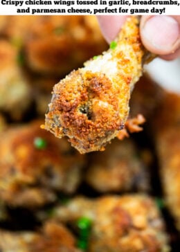 Pinterest pin with a hand holding a chicken wing over a plate with a pile of chicken wings topped with chives.