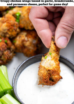 Pinterest pin with a hand dipping a chicken wing into a bowl of ranch, with celery and more chicken wings in the background.