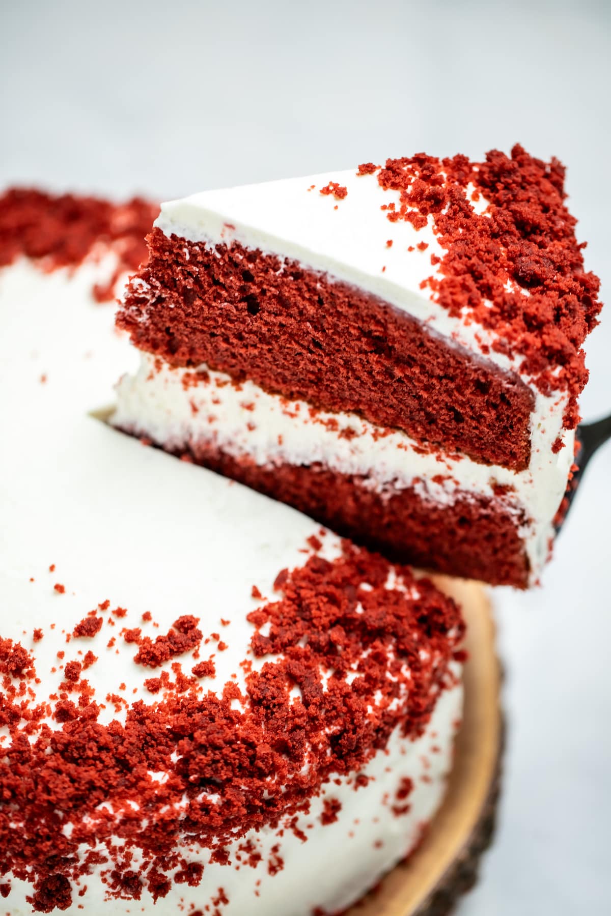 A double-layer gluten free red velvet cake on a wooden cake plate with a piece of cake being lifted up.