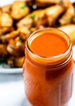 A mason jar full of homemade buffalo wing sauce in front of a plate of chicken wings.