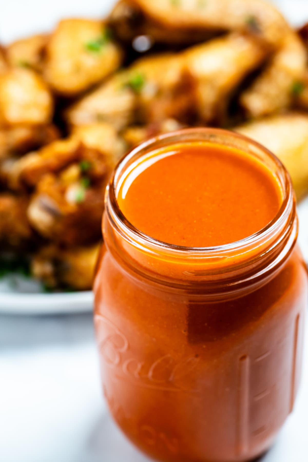 A mason jar full of homemade buffalo wing sauce in front of a plate of chicken wings.