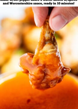 Pinterest pin with a hand holding a chicken wing after dipping it into a bowl of homemade buffalo wing sauce, with a plate of wings in the background.