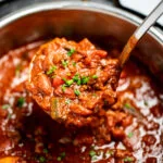 An instant pot of chili topped with chopped chives and a ladle scooping chili up.