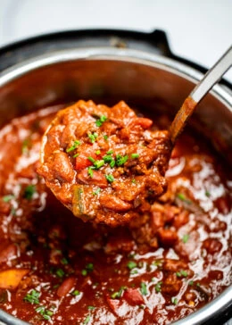 An instant pot of chili topped with chopped chives and a ladle scooping chili up.