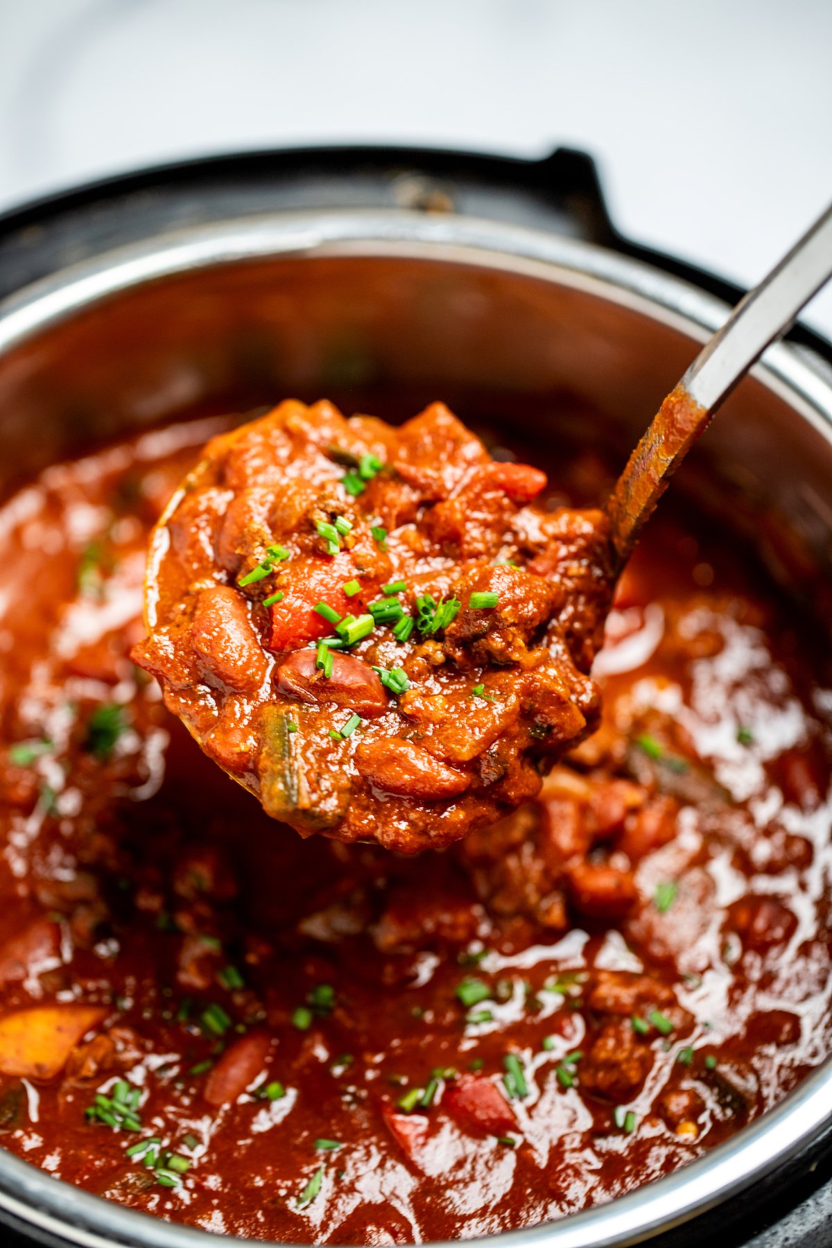 An instant pot of chili topped with chopped chives and a ladle scooping chili up.