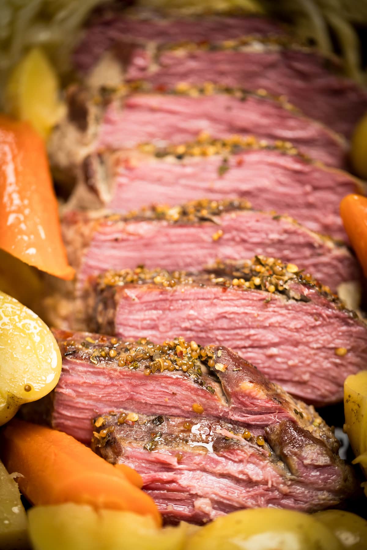 A closeup of sliced instant pot corned beef surrounded by potatoes and carrots.