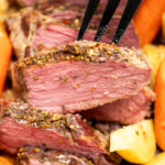 A closeup of sliced instant pot corned beef surrounded by potatoes and carrots, with a fork picking up a slice.