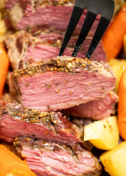 A closeup of sliced instant pot corned beef surrounded by potatoes and carrots, with a fork picking up a slice.