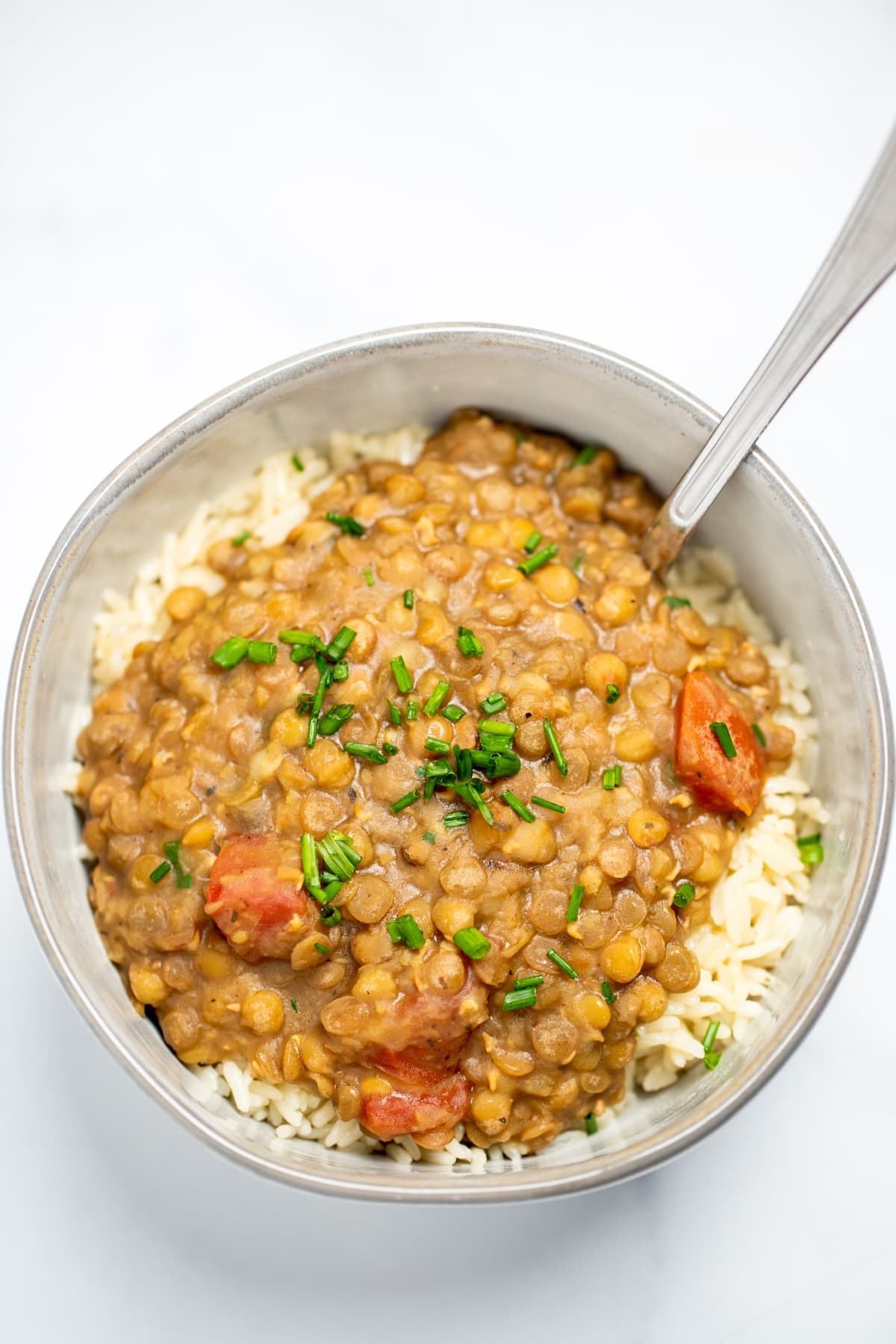 A bowl with rice topped with instant pot lentils and chives, with a spoon in the bowl, sitting on a table.