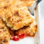 A spatula taking a piece of pineapple dump cake out of the baking dish.