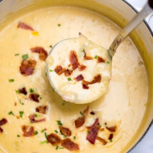 A dutch oven full of potato cheese soup topped with bacon and chives, with a ladle scooping up soup.